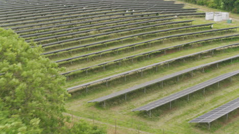 Sobrevuelo-Aéreo-De-Un-Gran-Panel-Solar-Fotovoltaico-En-Un-Verde-Campo-Templado