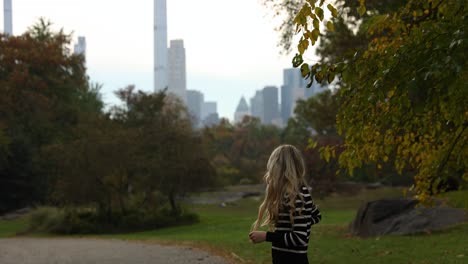 Blonde-woman-stand-in-New-York-city-central-park-with-skyscrapers-in-background