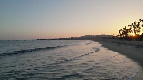 Drohne,-Die-Bei-Sonnenuntergang-Die-Küste-Von-Santa-Barbara,-Kalifornien,-Hinauffliegt,-Mit-Aufnahmen-Von-Meereswellen,-Die-Sanft-Gegen-Den-Strand-Schlagen,-Und-Von-Menschen,-Die-An-Der-Küste-Spazieren