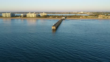 Point-of-interest-drone-shot-in-Florida-rotating-around-the-Lake-Worth-Pier-at-sunrise-looking-west-toward-the-beach-and-waterfront-homes