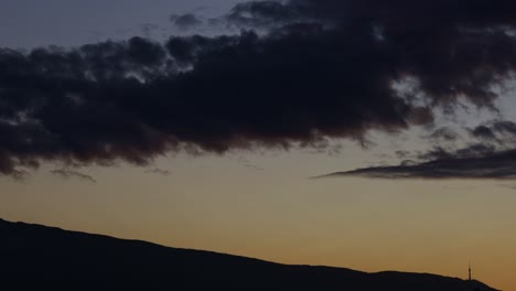 Timelapse-of-moving-clouds-above-a-mountain's-silhouette,-at-dusk