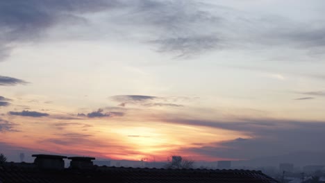Time-lapse-of-a-colorful-sunrise,-hidden-behind-clouds,-with-a-red-tile-roof-in-the-foreground