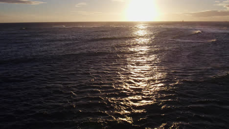 drone-shot-of-the-setting-sun-shining-across-the-rippling-ocean-waves-as-the-reflective-rays-follow-the-camera-movement