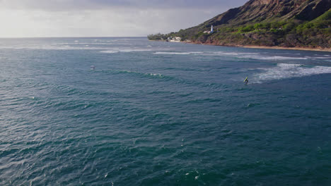 Drohnenaufnahmen,-Die-Sich-An-Einem-Sonnigen-Tag-In-Der-Nähe-Von-Diamond-Head-In-Hawaii-Auf-Die-Küste-Von-Oahu-Zubewegen,-Während-Surfer-Und-Kitesurfer-Die-Meeresoberfläche-übersäten