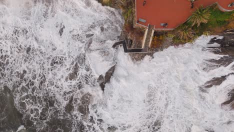 Nervi-coastline-in-genoa,-italy,-with-waves-crashing-against-rocks,-a-walkway-visible,-aerial-view