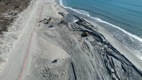 Drone-shot-of-beach-nourishment,-or-adding-sand-or-sediment-to-beaches-to-combat-erosion,-with-water-coming-out-of-pipe