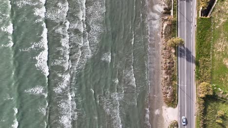 Top-down-aerial-footage-of-long-waves-on-a-beach-next-to-the-road