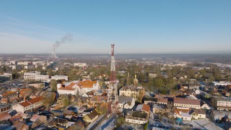 Aerial-establishing-view-of-Kuldiga-Old-Town-,-houses-with-red-roof-tiles,-sunny-winter-day,-travel-destination,-telecommunication-tower,-wide-drone-orbit-shot