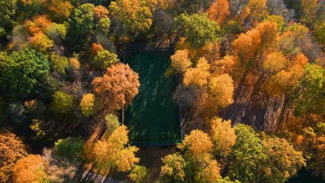 Drone-shot-of-a-soccer-playground-surrounded-by-colorful-vibrant-fall-trees-in-Kaunas,-Lithuania-in-autumn-time