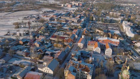 Aerial-establishing-view-of-Kuldiga-Old-Town-,-houses-with-red-roof-tiles,-sunny-winter-day,-travel-destination,-wide-drone-shot-moving-forward,-tilt-down