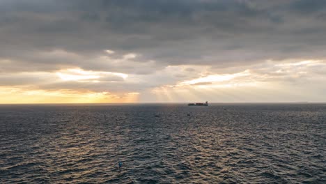 Sun-rays-piercing-through-clouds-over-the-ocean-near-Genoa-with-ships-on-the-horizon,-aerial-hyperlapse
