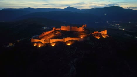 Drone-view-of-an-illuminated-castle-on-a-mountain-at-dusk