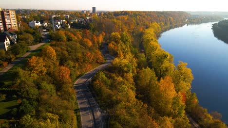 Drone-shot-of-a-car-driving-on-winding-road-alongside-Nemunas-River-in-Kaunas,-Lithuania,-zoom-in-shot