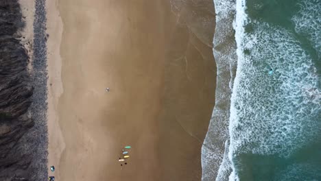 Drone-shot-of-the-coast-with-surfers-in-Arrifana-beach,-Portugal