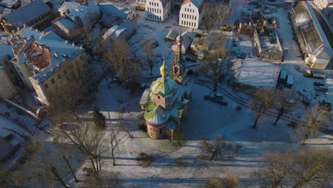 Aerial-establishing-view-of-Kuldiga-Old-Town-,-houses-with-red-roof-tiles,-orthodox-church,-sunny-winter-day,-travel-destination,-wide-drone-orbit-shot