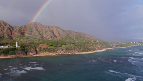 drone-footage-perfectly-catching-a-rainbow-against-the-volcanic-mountains-at-Diamond-Head-Lighthouse-on-the-island-of-Oahu-near-Honolulu-with-the-beautiful-blue-water-of-the-Pacific-ocean