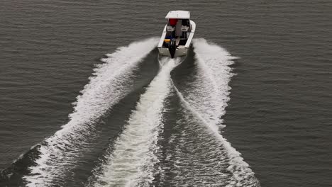 An-aerial-view,-following-a-small-white-boat-in-a-salt-marsh-off-the-south-shores-of-Long-Island,-NY-on-a-cloudy-day