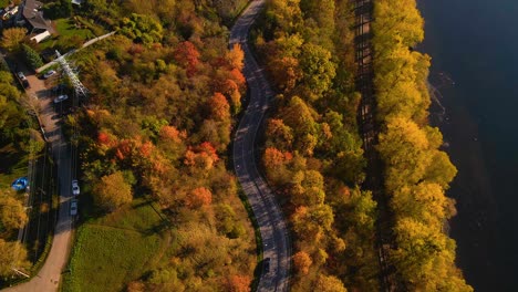 Aerial-shot-of-a-car-driving-on-winding-road-adjacent-to-railway-alongside-Nemunas-River-in-Kaunas,-Lithuania,-top-down-shot