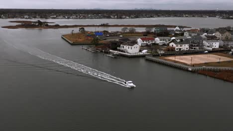 An-aerial-view-of-a-small-white-boat-in-the-bay-off-the-southern-shore-of-Freeport,-NY-on-a-cloudy-day