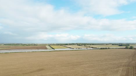 Aerial-drone-footage-on-the-east-coast-of-North-Yorkshire-flying-over-a-ploughed-farmer's-field-with-other-fields-and-sea-in-the-far-distance