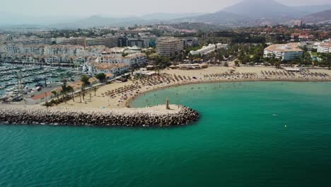 Puerto-Banus-beach-in-Marbella,-bustling-marina,-sandy-shores,-and-Mediterranean-Sea,-aerial-view