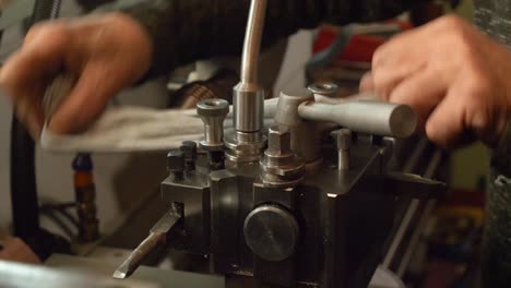 Caucasian-metal-worker-cleaning-part-of-a-lathe-machine-with-a-cloth,-detail-of-hands-and-the-workshop