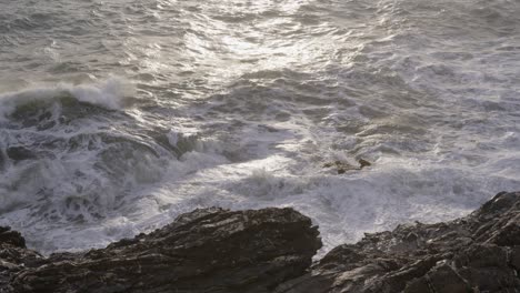 Waves-crash-against-rocky-shores-in-Nervi,-Genoa,-with-sunlight-reflecting-on-the-turbulent-sea