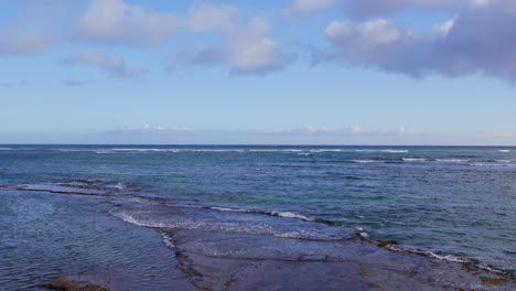 Die-Drohnenaufnahme-Erhebt-Sich-Schnell-Vom-Sandstrand,-Um-Den-Weiten-Blauen-Farbton-Des-Endlosen-Pazifischen-Ozeans-Und-Den-Blauen-Himmel-Mit-Bauschigen-Wolken-Am-Diamond-Head,-Oahu,-Hawaii,-Zu-Sehen
