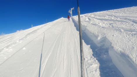 First-Person-Perspective:-Skiing-Uphill-on-a-Button-Lift-with-Skier-Ahead-Under-a-Clear-Blue-Sky
