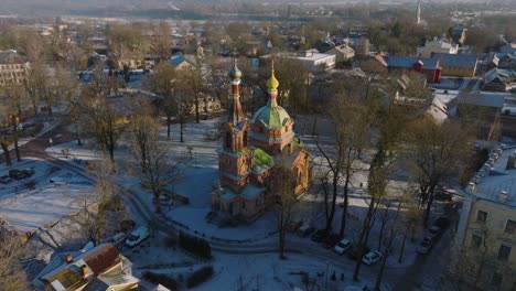 Aerial-establishing-view-of-Kuldiga-Old-Town-,-houses-with-red-roof-tiles,-orthodox-church,-sunny-winter-day,-travel-destination,-wide-drone-shot-moving-forward,-tilt-down