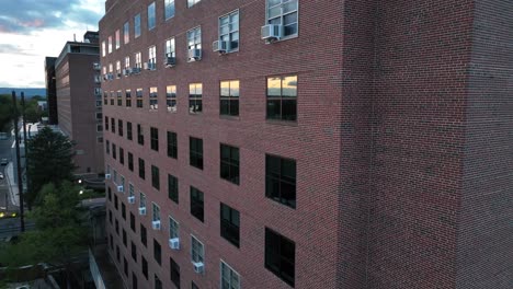 Brick-apartment-building-at-dusk,-reflecting-windows,-tree-shadows-on-facade,-clear-sky