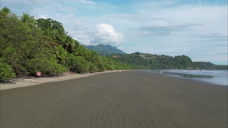 Flying-close-to-the-wet-sand-in-Costa-Rica-beach-during-low-tide-with-mountains-in-the-background