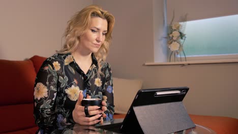 Blonde-haired-woman-viewing-her-tablet-holding-hot-drink