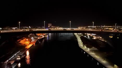 Cars-rush-over-bridge-at-night-as-Willemstad-comes-into-view-at-night,-aerial-dolly