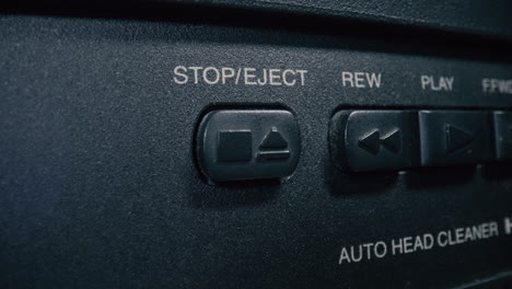 Close-up,-macro-shot-of-a-finger-pressing-the-'stop'-button-on-a-vintage-VCR-player's-control-panel