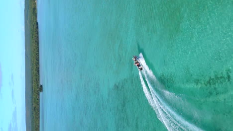 Aerial-follow-of-a-motorboat-by-the-Isle-of-Pines,-New-Caledonia's-crystal-clear-waters---vertical-video