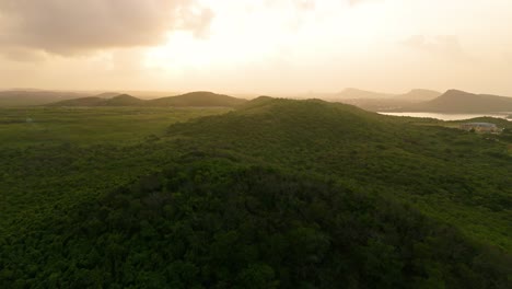 Golden-sunrise-light-spreads-across-lush-tropical-hills-of-Caribbean-island-Curacao,-aerial
