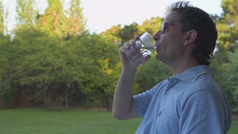 Hombre-Bebiendo-Agua-Y-Relajándose-En-El-Jardín-Con-Exuberante-Vegetación-En-Segundo-Plano.