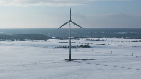 Windkraftanlage-In-Einer-Verschneiten-Landschaft-Mit-Entfernten-Bäumen-Und-Feldern