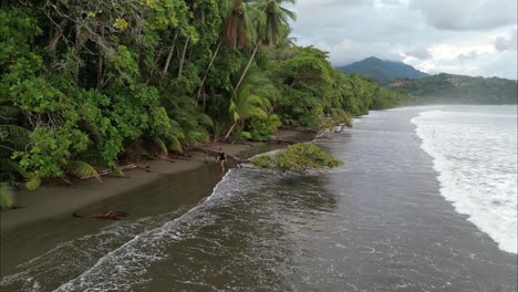 Mann,-Der-Bei-Ebbe-In-Costa-Rica-über-Einen-Baumstamm-Am-Strand-Läuft