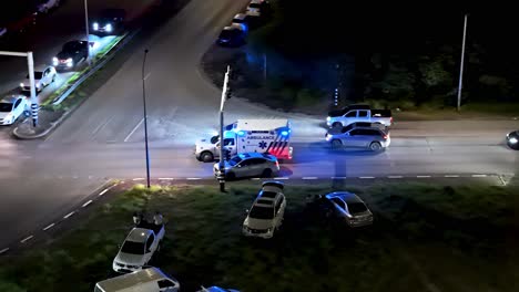 Ambulance-with-flashing-blue-lights-weaves-between-cars-on-busy-road,-aerial-drone-tracking-at-night