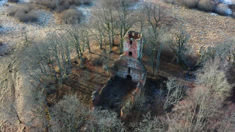 Drone-view-above-abandoned-church-bell-tower-and-wall-remains,-bare-tree-around