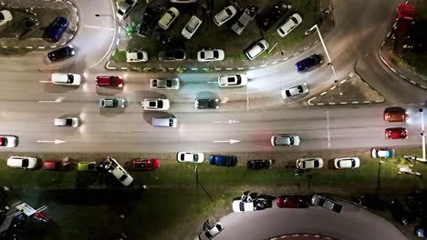 Drone-ascends-above-cars-parked-on-grass-median-and-turning-onto-on-ramp-at-night