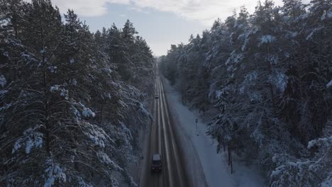 Drone-flight-over-cars-driving-through-a-snow-laden-Baltic-forest-road