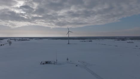 Aerial-orbit-of-a-lone-wind-turbine-in-a-vast-snowy-Baltic-landscape-under-a-cloudy-sky