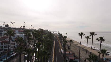 Aerial-View-of-California-beach-town-with-surfers-crossing-bridge-over-train-tracks