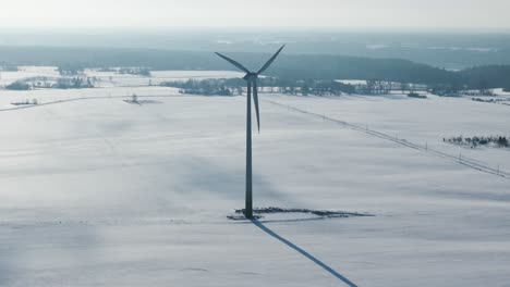 Zeitlupe-Einer-Windkraftanlage,-Die-Sich-In-Einer-Weiten-Verschneiten-Landschaft-Mit-Entfernten-Bäumen-Und-Feldern-Dreht
