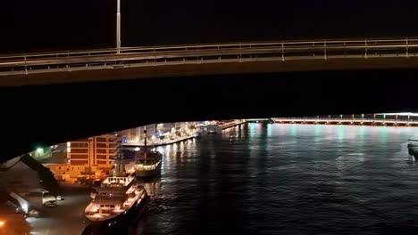 Curved-Juliana-bridge-frames-Handelskade-as-cars-rush-by-at-night,-aerial-overview