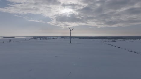 Drohne-Umkreist-Eine-Einsame-Windkraftanlage-Inmitten-Einer-Schneebedeckten-Ostseelandschaft-Unter-Einem-Düsteren-Himmel