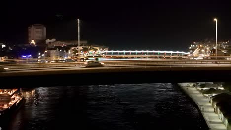 Aerial-ascend-above-bridge-reveals-Willemstad-Curacao-at-night-shimmering-lights-reflect-on-water